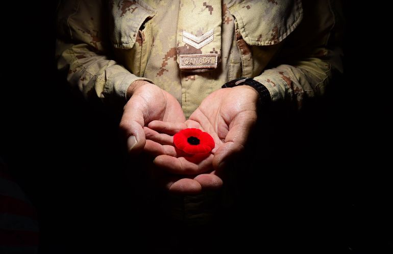 Mani di soldato che offrono un papavero rosso simbolico