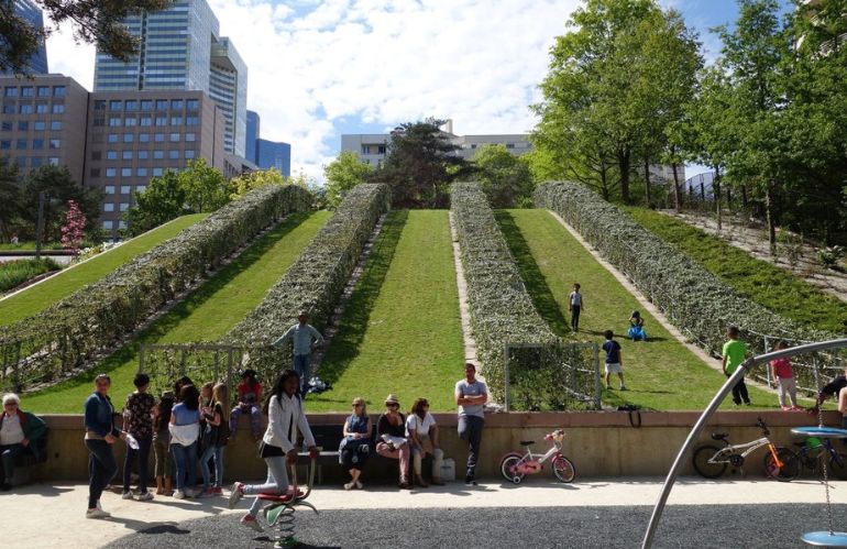 Vista su un parco urbano progettato da Allain Provost, con vialetti curvi, vegetazione rigogliosa e figura umana di spalle